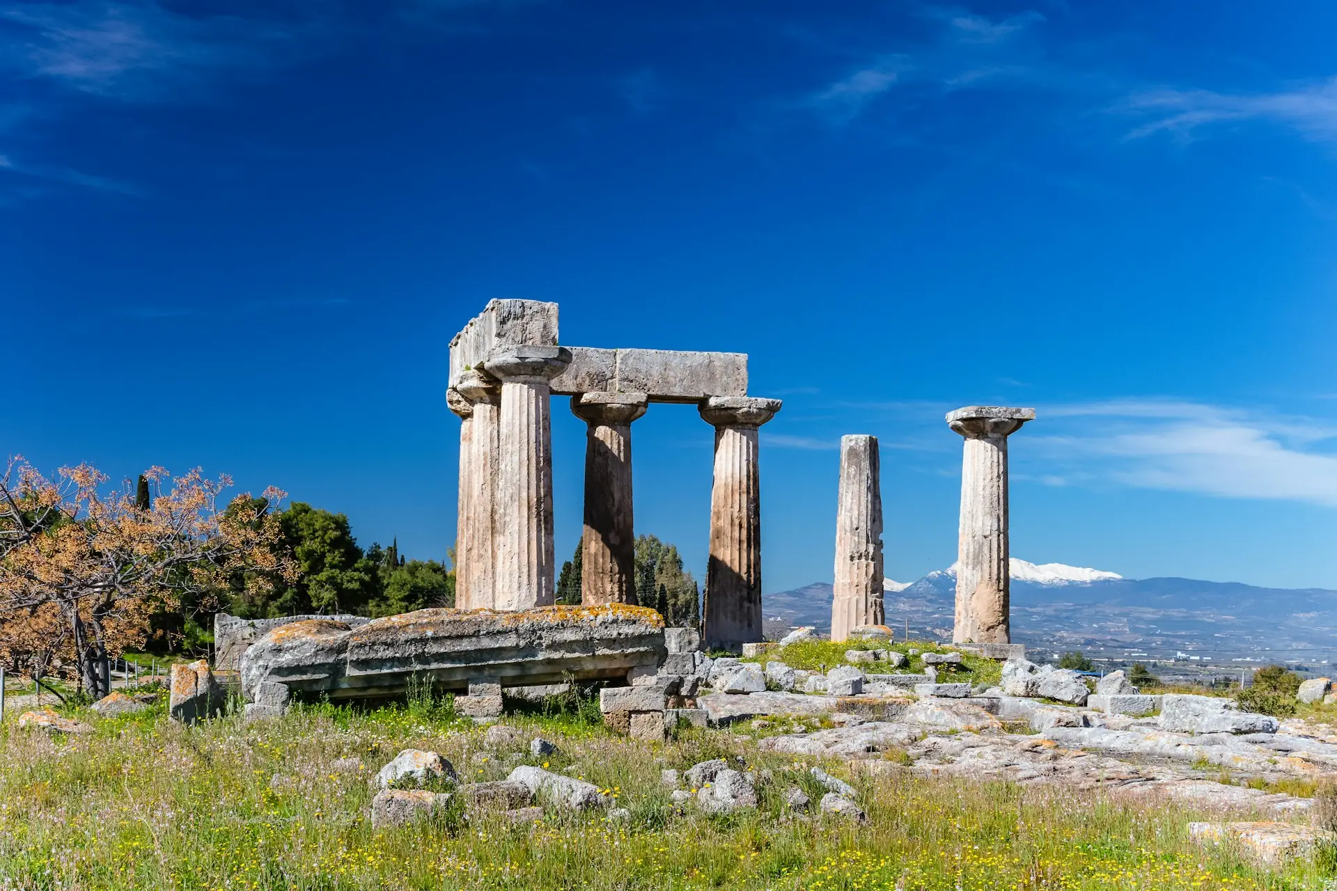 Ancient Corinth ruins with standing stone columns and mountains in the background under a clear blue sky.