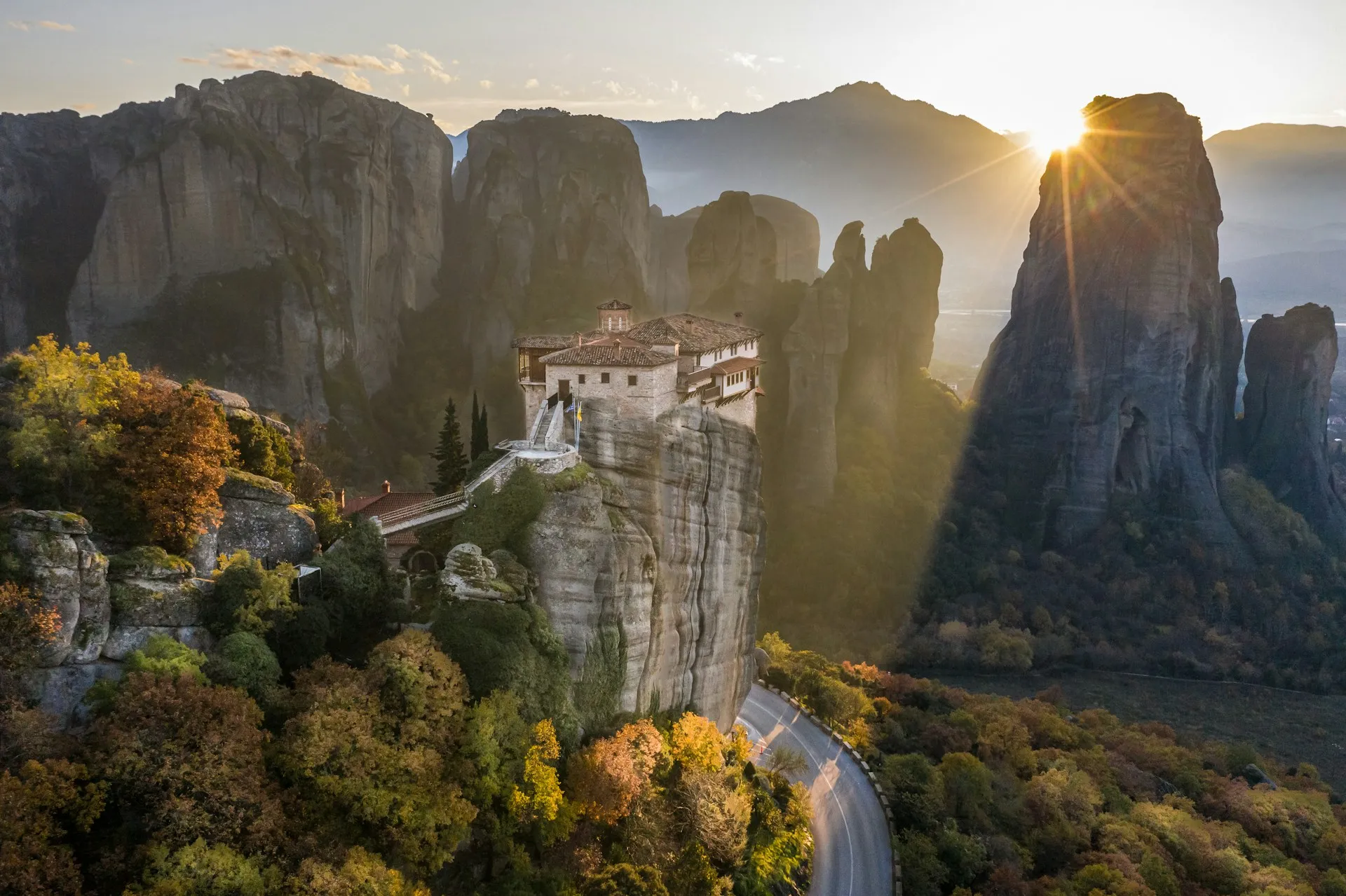 Monastery at Meteora standing on a tall rock pillar at sunset, surrounded by towering cliffs.
