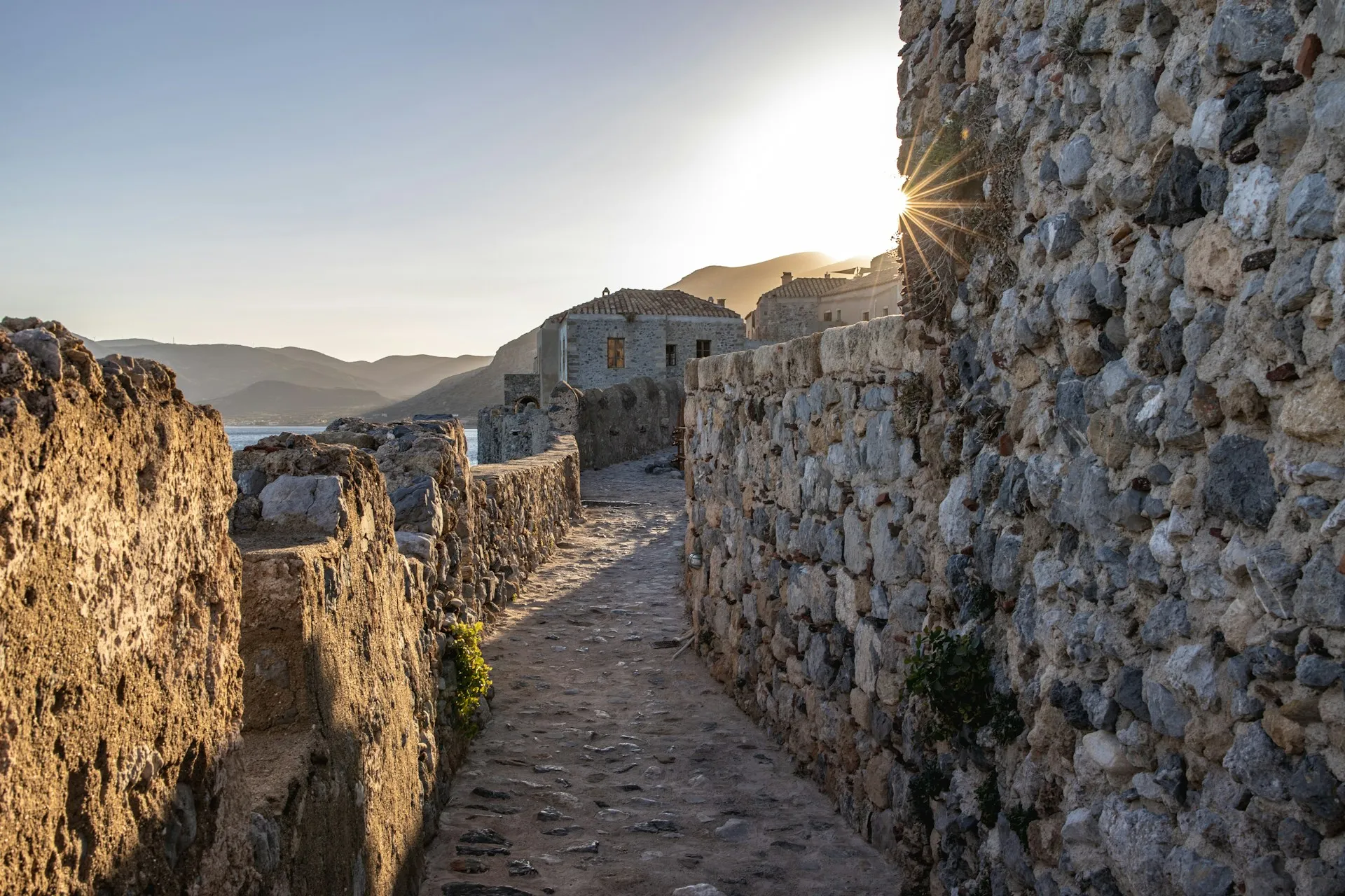Stone alley inside the fortified town of Monemvasia with the sea and hills beyond.